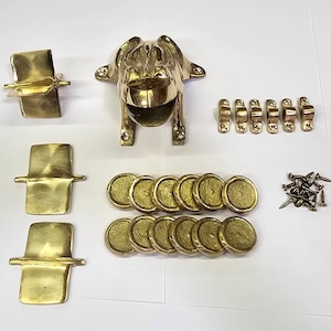 May include: A brass frog figurine with a wide open mouth, 18 round brass discs, 8 brass brackets, and a pile of screws. The frog is a wall mount and the discs are likely for a decorative wall project.