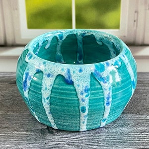 May include: A white ceramic mug with a black handle and the text "But First, Coffee" in a bold, black font. The mug is set against a blurred background, suggesting a cozy setting.