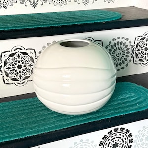 May include: A spherical ceramic vase with a glossy off-white finish and horizontal ribbed detailing. The vase features a circular opening at the top and a smooth, rounded body that tapers slightly toward the base, showcasing a clean, simple design.