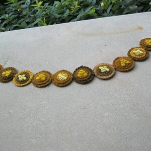May include: A brown and yellow felt garland with a bee design. The garland is strung on a black cord and has nine felt circles.