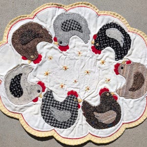 May include: A handmade, scalloped-edge trivet featuring seven appliqued chickens in various tweed patterns. The chickens have red combs and yellow beaks, set against a white background with embroidered star accents. The trivet is trimmed with red and yellow stitching.