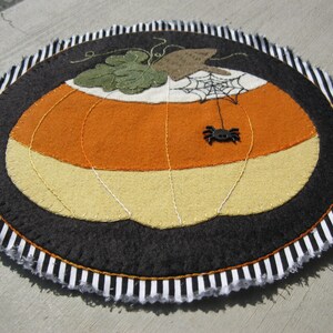 May include: A black and white striped felt pumpkin with a spider and web on top. The pumpkin is orange and yellow with a green stem.