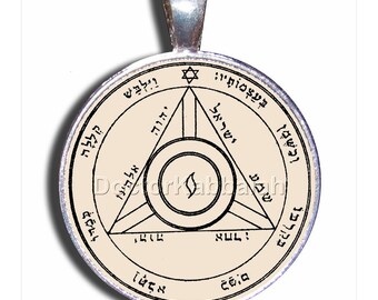 Puede incluir: Un colgante de plata con un disco circular de color crema que presenta un triángulo negro con texto hebreo en su interior. El triángulo está rodeado por un círculo con texto hebreo y una estrella de David.