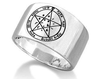 May include: A wide, silver-colored ring with a circular design featuring a five-pointed star and text. The ring has a polished finish and a thick band. The design is in black and is centered on the ring's top surface.