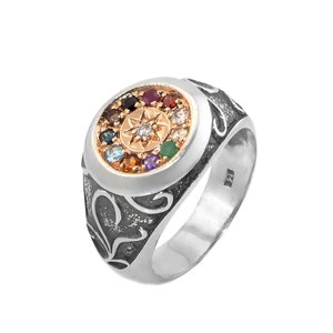 May include: A silver ring with a round, multi-colored gemstone setting. The ring has a detailed, ornate design and a gold-toned center with a star-shaped design.