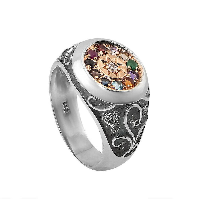 May include: A silver ring with a round, multi-colored gemstone setting. The ring features a detailed, ornate design and a star-shaped center stone.