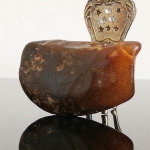 May include: A small, brown, irregularly shaped rock with a silver chair-shaped ornament on top. The ornament has a decorative design and rhinestones.