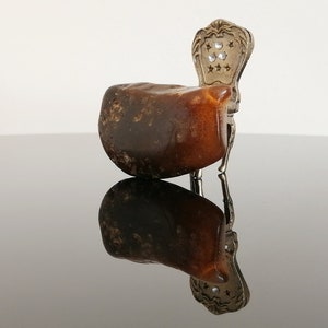 May include: A small, dark brown, irregularly shaped rock sits on a silver chair with a decorative back. The chair is on a black reflective surface.
