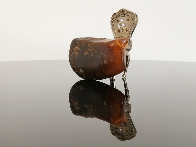 May include: A small, dark brown, irregularly shaped rock sits on a silver chair with a decorative back. The chair is on a black reflective surface.