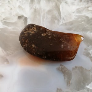 May include: A dark brown amber stone with a smooth, polished surface. The stone has a slightly irregular shape and is translucent.