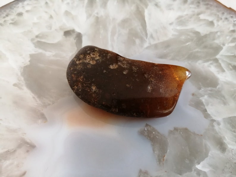 May include: A dark brown amber stone with a smooth, polished surface. The stone has a slightly irregular shape and is translucent.