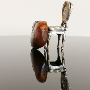 May include: A miniature silver chair with a brown wooden seat. The chair is sitting on a black reflective surface.