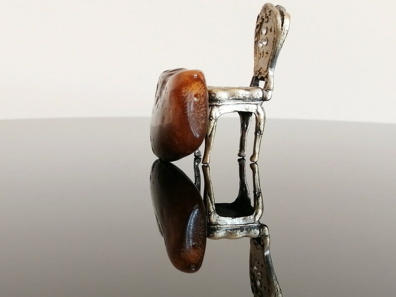 May include: A miniature silver chair with a brown wooden seat. The chair is sitting on a black reflective surface.