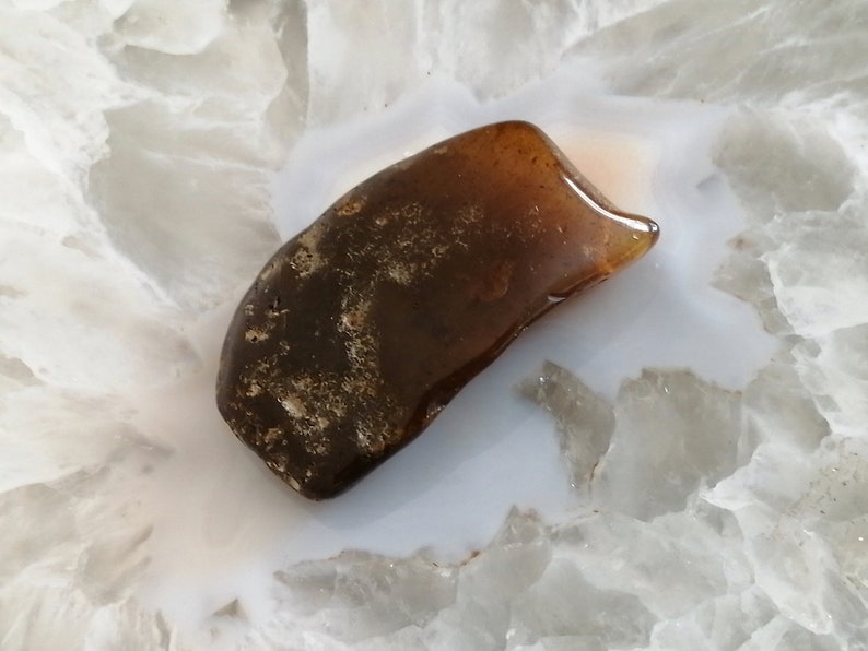 May include: A dark brown, irregularly shaped piece of amber on a white, textured surface.