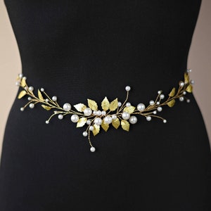 May include: A gold and white beaded belt with a floral design. The belt is made of gold wire and has small white pearls attached to it. The floral design is made of gold leaves and has a delicate and feminine look.