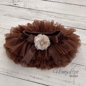 May include: Brown tulle baby bloomers with a brown satin bow and a beige flower with a pearl embellishment. The bloomers are layered and have a ruffled edge. The text "Honey Love Boutique" is visible in the bottom right corner of the image.
