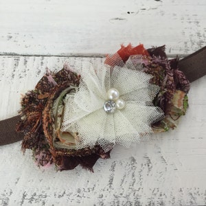 Op de afbeelding: Een bruine, roze en oranje bloemen van stof met een witte tule overlay en parel accenten. De bloem is bevestigd aan een bruin hoofdband.
