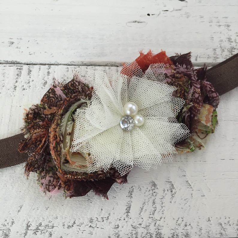 Op de afbeelding: Een bruine, roze en oranje bloemen van stof met een witte tule overlay en parel accenten. De bloem is bevestigd aan een bruin hoofdband.