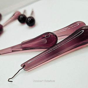 May include: A set of purple glass teardrop-shaped ornaments with wire loops. The ornaments are approximately 4 inches long.