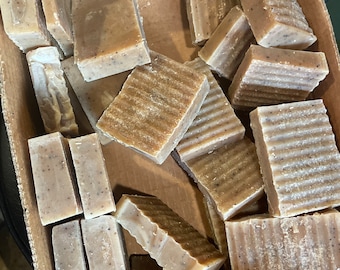 May include: A box filled with handmade bars of soap. The soap is a light brown color and has a textured surface.