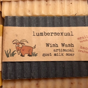 May include: A bar of goat milk soap with a black and white label. The label says "lumbersexual Wish Wash artisanal goat milk soap" and has a cartoon goat on it. The soap is hand-crafted in small batches.