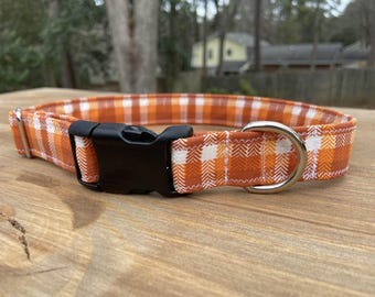 May include: Orange and white plaid dog collar with a black buckle and silver D-ring.