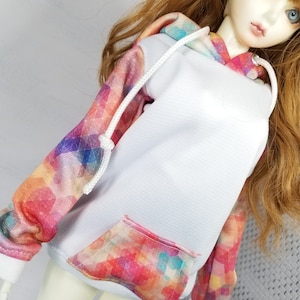 May include: A white hoodie with a colorful geometric pattern on the sleeves and pocket. The hoodie has a drawstring hood and a kangaroo pocket.