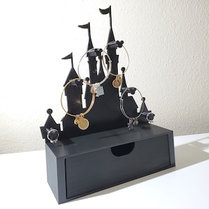 May include: Black castle-shaped jewelry organizer with a drawer. The organizer has five hooks for hanging bracelets and a small compartment for rings.