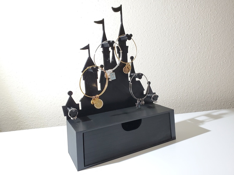 May include: Black castle-shaped jewelry organizer with a drawer. The organizer has five hooks for hanging bracelets and a small compartment for rings.