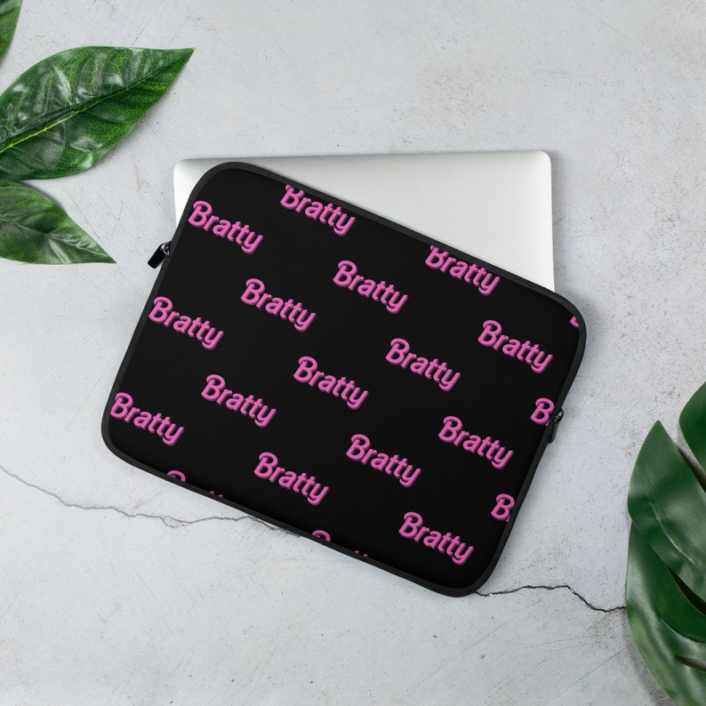 Puede incluir: Funda para port&aacute;til negra con un patr&oacute;n repetido rosa de la palabra "Bratty".