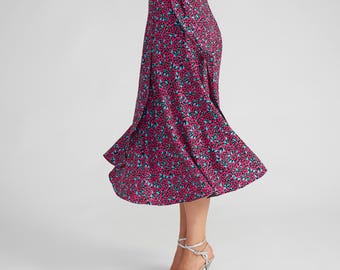 May include: A midi-length wrap skirt featuring a vibrant floral pattern with small pink, magenta, and teal blue blossoms set against a black background. The skirt has a high-waisted design with a side tie closure and a flared, flowing silhouette.