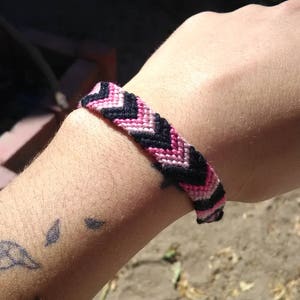 Może przedstawiać: Bransoletka przyjaźni w kolorze różowym, czarnym i białym z wzorem w chevron.