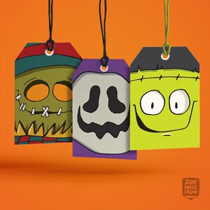 May include: Three Halloween-themed gift tags with black string. The tags feature cartoon faces of a zombie, a ghost, and Frankenstein's monster. The zombie tag is green, the ghost tag is purple, and the Frankenstein tag is lime green. The background is orange.