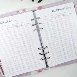 May include: A white planner with a purple cover and a pink and white checked pattern. The planner is open to a page with the title "ASSIGNMENT Tracking" and columns for unit name, date due, % of total grade, date submitted, and final grade.