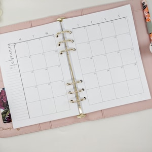 May include: A pink leather bound planner with gold rings and a white monthly calendar insert for February 2021. The calendar has the days of the week labelled M, T, W, T, F, S, S.