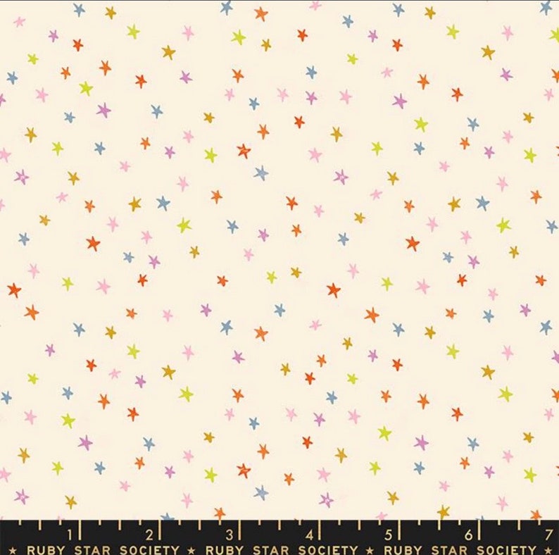 May include: A white fabric with a repeating pattern of small, colourful stars. The stars are in shades of yellow, orange, pink, and blue.