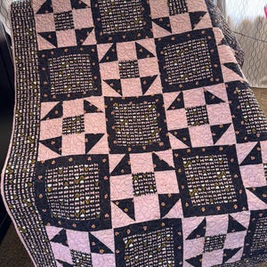 May include: A handmade quilt with a patchwork design. The quilt features a pattern of alternating pink and navy blue squares and triangles. The navy blue squares have a floral pattern. The quilt is folded over a chair.