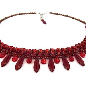 Könnte beinhalten: Eine rote Perlenkette mit einem Tropfenmuster. Die Kette besteht aus kleinen roten Perlen und größeren tropfenförmigen Perlen.