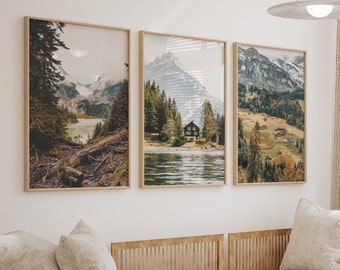 May include: Three framed landscape art prints depicting mountain and lake scenes hang above a beige sectional sofa. The prints feature natural tones of green, brown, and blue. A round wooden coffee table and decorative items complete the living room setting.