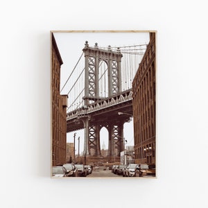 May include: A view of the Manhattan Bridge in New York City, with cars driving on the street below. The bridge is a steel structure with a grey colour and a large arch in the centre. The buildings on either side of the bridge are brown brick.
