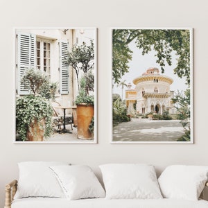 May include: Two framed prints of architectural scenes. The first print shows a patio with a table and chairs, surrounded by lush greenery. The second print shows a white building with a domed roof, surrounded by trees and a paved path.