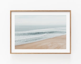 May include: A framed photograph of a beach scene with blue water and white waves crashing on a sandy shore. The sky is a light blue and the horizon is visible in the distance.