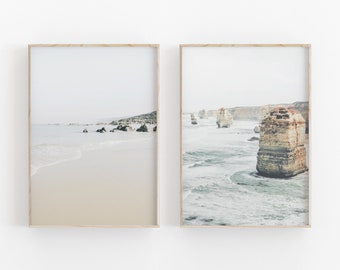 以下が含まれることがあります： ビーチのシーンを写した額装された写真が2枚。左の写真は、砂浜に波が打ち寄せ、遠くには岩場が見える。右の写真は、岩場が海から突き出ている岩だらけの海岸線が見える。