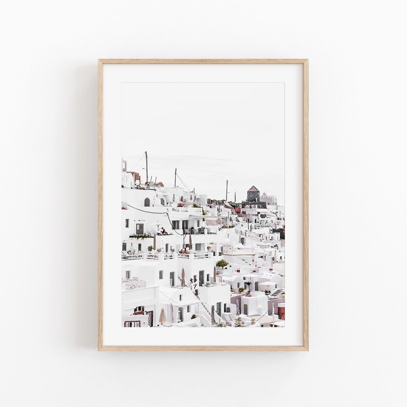 May include: A photograph of a white village built on a hillside. The buildings are all white with blue accents and there are many windows and balconies. The village is located in a sunny, warm climate.