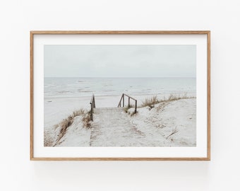 May include: A wooden walkway leads to a sandy beach with a blue ocean in the background. The sky is a light blue and the sand is white.