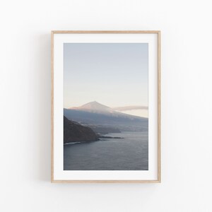 以下が含まれることがあります： 遠くの山脈と頂上を望む、水域を見下ろす写真が額装されています。空は薄い青色で、雲が少しあります。