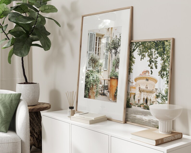 May include: Two framed photographs on a white shelf. The left photo shows a Parisian courtyard with a potted plant and a table and chairs. The right photo shows a building with a dome and a lush green tree.