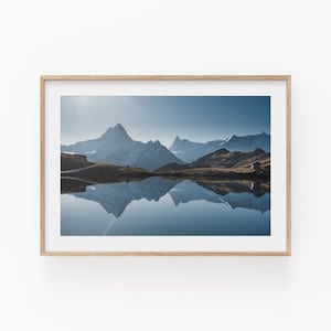 May include: A framed photograph of a mountain range reflected in a still lake. The mountains are snow-capped and the lake is a deep blue. The sky is a clear blue.