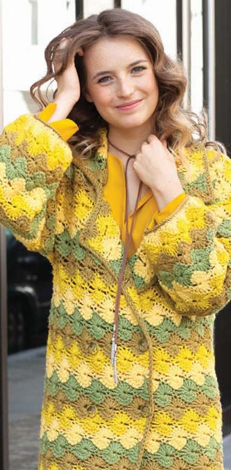 K&ouml;nnte beinhalten: Eine geh&auml;kelte Strickjacke in Gelb, Gr&uuml;n und Braun mit einer braunen Lederschnur. Die Strickjacke hat einen Knopfverschluss und ein gewelltes Design.