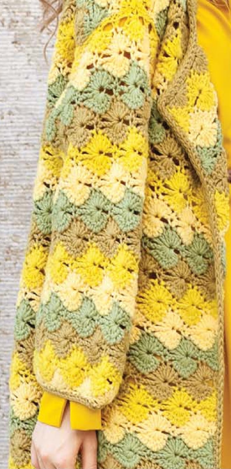 K&ouml;nnte beinhalten: Eine geh&auml;kelte Strickjacke in einem gelben, gr&uuml;nen und braunen Farbmuster. Die Strickjacke hat eine lockere Passform und einen langen, offenen Vorderteil.
